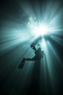 A scuba diver ascends into the light emanating above A scuba diver ascends into the light emanating above