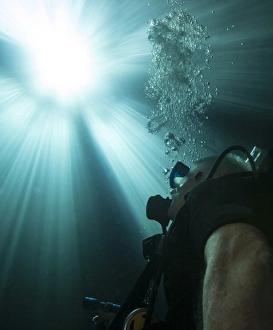 A scuba diver surfacing and looking up into the light A scuba diver surfacing and looking up into the light