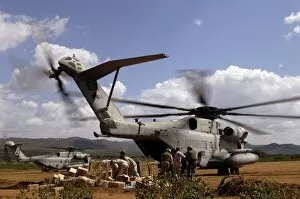 Soldiers and sailors help pile boxes of food and water off a CH-53E helicopter