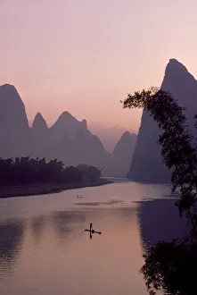 Man using pole to propel bamboo raft on Lijang / Li River, Karst peaks beyond. At dawn Man using pole to propel bamboo raft on Lijang / Li River, Karst peaks beyond. At dawn