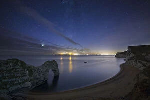 Stars and Milky Way over Durdle Door and the Jurassic Coast, with the lights of Weymouth
