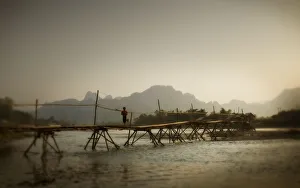 Boy Running Across A Wooden Bridge On A River With Mountains In The Background; Vang Vieng Laos Boy Running Across A Wooden Bridge On A River With Mountains In The Background; Vang Vieng Laos
