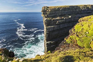 Cliff Face Rock Formation In Ocean With Waves, Blue Sky And Clouds; Kilkee, County Clare, Ireland Cliff Face Rock Formation In Ocean With Waves, Blue Sky And Clouds; Kilkee, County Clare, Ireland
