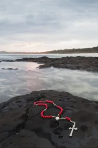A Cross And Rosary Beads Laying On A Rock At Flat Rock; Ballina, New South Wales, Australia A Cross And Rosary Beads Laying On A Rock At Flat Rock; Ballina, New South Wales, Australia