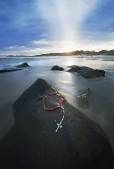 A Cross And Rosary Beads Laying On A Rock At Flat Rock; Bellina, New South Wales, Australia A Cross And Rosary Beads Laying On A Rock At Flat Rock; Bellina, New South Wales, Australia