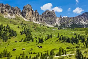 Grassy mountain side with wooden mountain huts and the jagged mountain ridge at the Gardena Pass in the Dolomites in