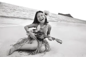 Hawaii, Oahu, Young Girl Smiling And Playing Ukulele On The Beach In A Hula Skirt Hawaii, Oahu, Young Girl Smiling And Playing Ukulele On The Beach In A Hula Skirt
