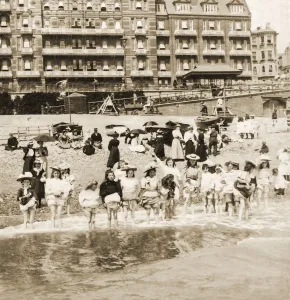 Historic image in sepia of a group of children standing in a row in shallow water with their skirts Historic image in sepia of a group of children standing in a row in shallow water with their skirts