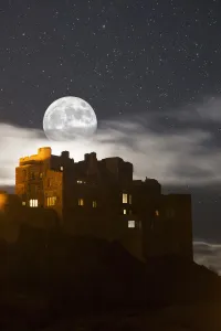Full Moon Glowing In A Starry Sky Over Illuminated Buildings; Bamburgh, Northumberland, England Full Moon Glowing In A Starry Sky Over Illuminated Buildings; Bamburgh, Northumberland, England