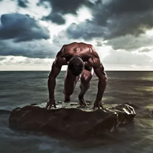 A muscular man in the starting position on a wet rock in the water; Tarifa cadiz andalusia spain A muscular man in the starting position on a wet rock in the water; Tarifa cadiz andalusia spain