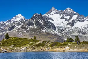 People hiking along the shore of the small mountain lake Grunsee with mountain tops of the Swiss Alps in the background People hiking along the shore of the small mountain lake Grunsee with mountain tops of the Swiss Alps in the background