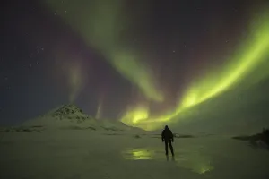 A Person Stands On The Frozen Blackstone River Beneath The Northern Lights; Yukon, Canada A Person Stands On The Frozen Blackstone River Beneath The Northern Lights; Yukon, Canada