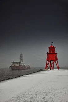 A Red Lighthouse Along The Coast In Winter With A Boat Off The Shore In The Water; South Shields, Tyne And Wear A Red Lighthouse Along The Coast In Winter With A Boat Off The Shore In The Water; South Shields, Tyne And Wear