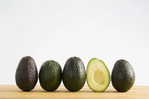 A Row Of Avocados Standing Upright On A Wooden Board With One Cut In Half Without The Pit; Calgary, Alberta, Canada A Row Of Avocados Standing Upright On A Wooden Board With One Cut In Half Without The Pit; Calgary, Alberta, Canada