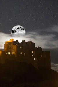 Santa In His Sleigh And Reindeer Silhouetted In The Starry Sky In Front Of The Moon Over Buildings; Bamburgh Santa In His Sleigh And Reindeer Silhouetted In The Starry Sky In Front Of The Moon Over Buildings; Bamburgh