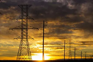 Silhouette Of Large Metal Powerline Towers With Colourful Clouds And Sun; Calgary Silhouette Of Large Metal Powerline Towers With Colourful Clouds And Sun; Calgary