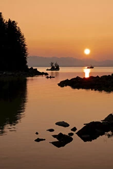 Silhouette of trawlers and a small boat along the rocky shoreline with a glowing sunset, Alaska, USA
