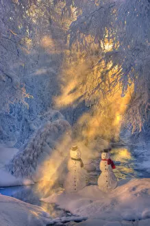 Snowman Couple Standing Next To A Stream With Sunrays Shining Through Fog And Hoar Frosted Trees In The Background