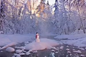 Snowman Standing On A Small Island In The Middle Of A Stream With Sunrays Shining Through Fog And Hoar Frosted Trees In