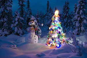 Snowman Stands In A Snowcovered Spruce Forest Next To A Decorated Christmas Tree In Wintertime Snowman Stands In A Snowcovered Spruce Forest Next To A Decorated Christmas Tree In Wintertime