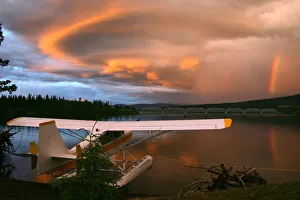 Sunlit Storm Clouds Over A Float Plane With Rainbow And Teslin Bridge In Background, Teslin Lake, Yukon Sunlit Storm Clouds Over A Float Plane With Rainbow And Teslin Bridge In Background, Teslin Lake, Yukon
