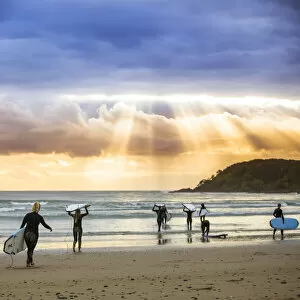 Surfers heading out to catch a wave at sunrise, Arrawarra, New South Wales, Australia