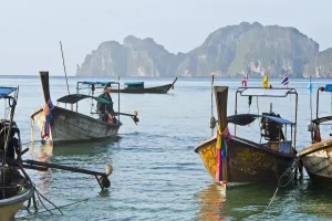 Thailand, Koh Phi Phi, Longtail boats along the shoreline, Mountains in distance Thailand, Koh Phi Phi, Longtail boats along the shoreline, Mountains in distance