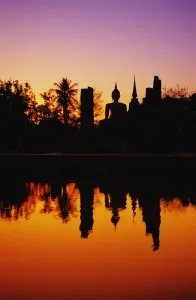 Thailand, Sukhothai, Wat Mahathat, Distant View Of Buddha Statue At Sunset, Silhouetted And Reflecting On Water Thailand, Sukhothai, Wat Mahathat, Distant View Of Buddha Statue At Sunset, Silhouetted And Reflecting On Water