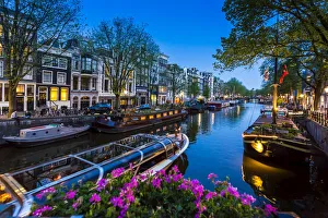 Tour boat travelling along the canal with houseboats moored along the seawall of the Keizersgracht in the enveing in Tour boat travelling along the canal with houseboats moored along the seawall of the Keizersgracht in the enveing in