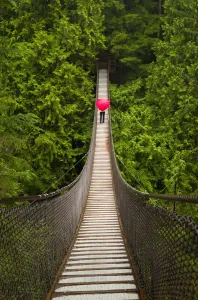 Woman With A Red Heart-Shaped Umbrella Crossing The Lynn Canyon Suspension Bridge, North Vancouver; Vancouver Woman With A Red Heart-Shaped Umbrella Crossing The Lynn Canyon Suspension Bridge, North Vancouver; Vancouver