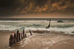 Wooden Posts On A Beach With A Boat Being Tossed In The Water And Waves Crashing Wooden Posts On A Beach With A Boat Being Tossed In The Water And Waves Crashing