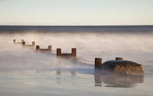 Wooden Posts And Boulders Immersed In Water At The Coast; Northumberland, England Wooden Posts And Boulders Immersed In Water At The Coast; Northumberland, England
