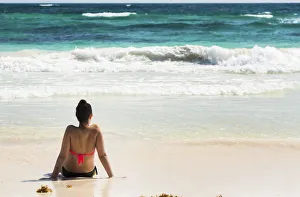 Young Woman Sitting On Sandy Beach In Water Looking Out At Waves Coming In And Blue Sky; Akumal, Quintana Roo, Mexico Young Woman Sitting On Sandy Beach In Water Looking Out At Waves Coming In And Blue Sky; Akumal, Quintana Roo, Mexico