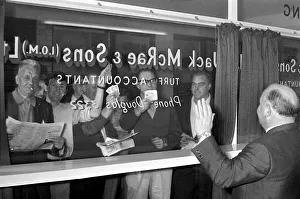 Occupations Gallery: Bookmaker Sidney Glanz waves to punters waving cash at him through a glass window inside