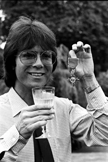 Images Dated 23rd July 1980: Cliff Richard with his OBE medal award drinkng wine 1980