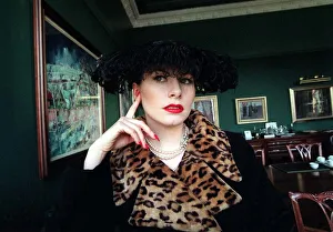 Evita Fashion Model sitting down black coat with leopard skin collar feather hat black Evita Fashion Model sitting down black coat with leopard skin collar feather hat black