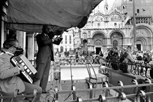 General scenes in Venice. Fiddling while Venice sinks. Signor Ninor Brunello leads a