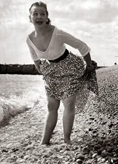 A girl wearing a flowery skirt and white top as she paddles in the waters of a shingle A girl wearing a flowery skirt and white top as she paddles in the waters of a shingle