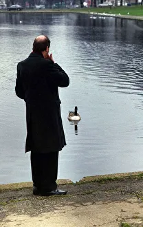 Gorden Kaye actor looking out over a boating lake in a park with duck paddling towards Gorden Kaye actor looking out over a boating lake in a park with duck paddling towards
