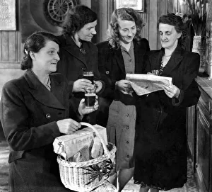 A group of women standing reading the newspaper, one woman in the foreground holding a A group of women standing reading the newspaper, one woman in the foreground holding a