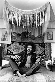 Icons Collection: Jimi Hendrix, world famous guitarist, sitting on bed wearing open shirt and necklace