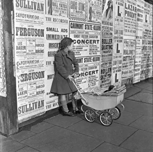 Little girl with toy pram stands waiting for her mother against a background of adverts Little girl with toy pram stands waiting for her mother against a background of adverts