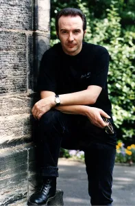 Midge Ure pop singer foot up arms on knee outside house black jeans T shirt Midge Ure pop singer foot up arms on knee outside house black jeans T shirt