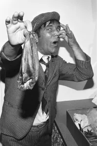 Prints of Comedian Norman Wisdom seen here in the persona of hapless on screen character Norman Pitkin in his dressing room in Douglas on the Isle of Man holding a kipper. 28th August 1977 Isle Of Man Prints: Norman Wisdom as Norman Pitkin, Isle of Man Print 1977