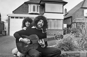 Print of Jeff Lynne sitting in a driveway with an acoustic guitar