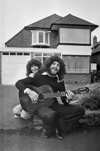 01400 Prints: Jeff Lynne plays acoustic guitar in a driveway with an unidentified woman