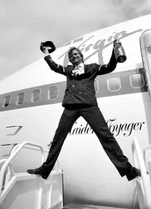 Images Dated 21st June 1984: Richard Branson holding a bottle of champagne and pilots hat as he celebrates Virgin