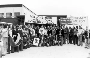 Rugby fans welcome the British Lions home to Heathrow. The banner on the right refers to Rugby fans welcome the British Lions home to Heathrow. The banner on the right refers to