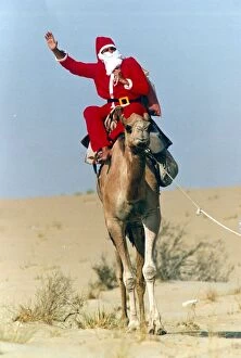 Images Dated 3rd December 1990: Santa Claus waves from atop his camel in the desert on his way to delivering a message to