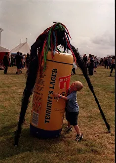 Stilted figure at T in the Park wearing a bright coloured wig standing over an inflatable Stilted figure at T in the Park wearing a bright coloured wig standing over an inflatable